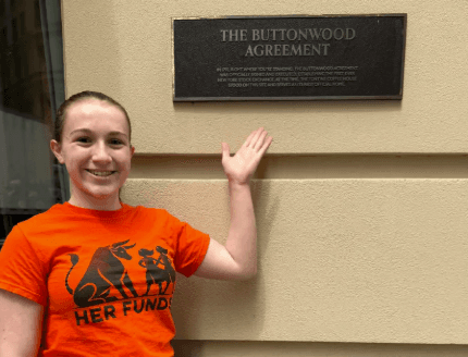 Sophia DeGregorio pointing to the Buttonwood Agreement plaque on Wall Street
